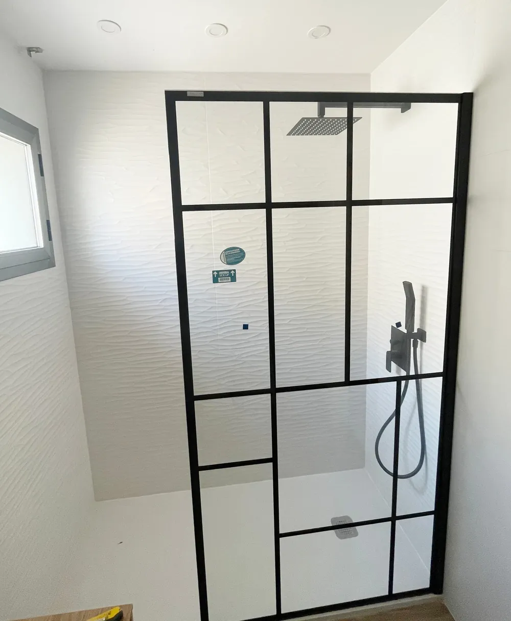 Mampara de ducha de perfil negro tipo cuadrícula sobre pared blanca
