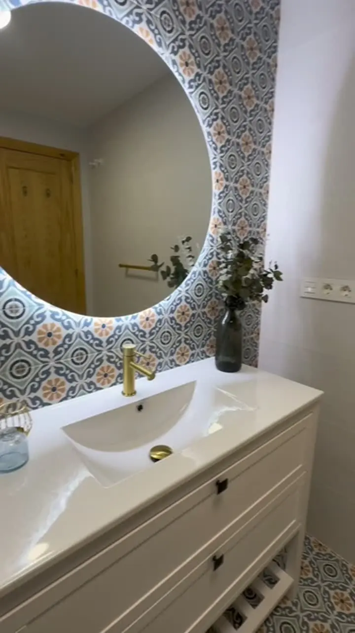 Baño Ulises: espejo circular retroiluminado sobre mueble blanco y pared de azulejo hidráulico